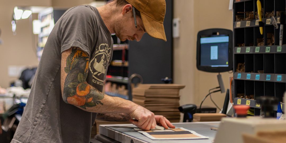 A Miller's craftsperson finishing a printed piece by hand at a bindery bench in the lab