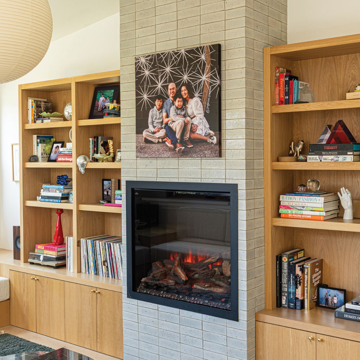 A large family portrait print mounted above a fireplace in a living room lined with oak bookshelves