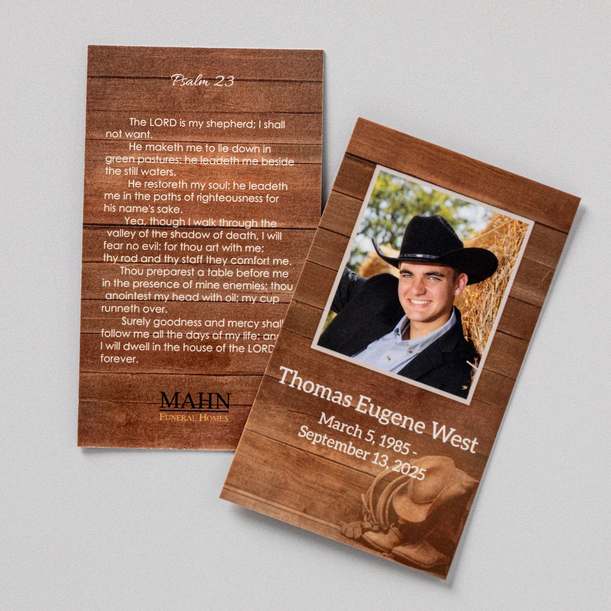 Front and back of a personalized memorial prayer card on a wood grain design — a photograph, name, and dates on the front, Psalm 23 and the funeral home logo on the back