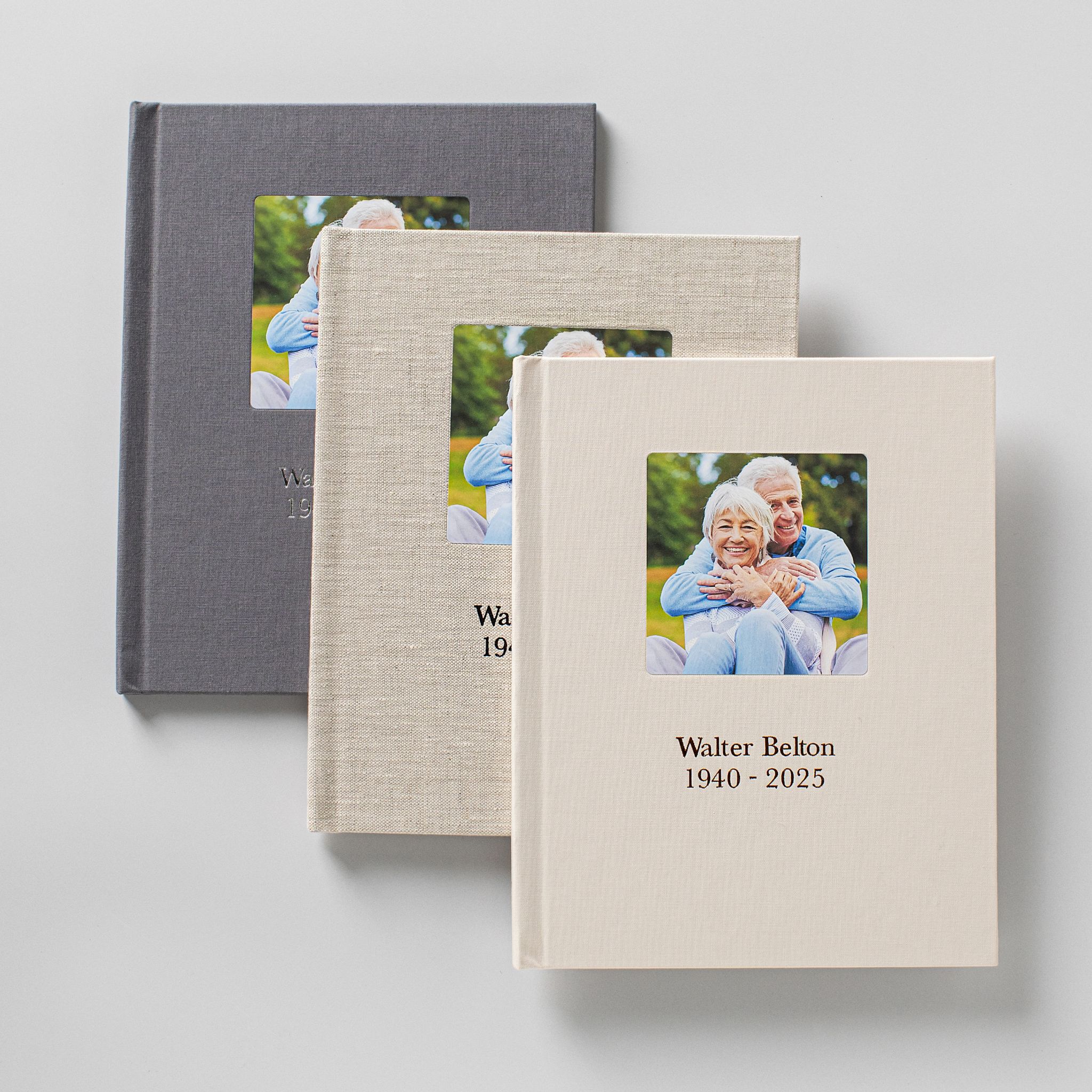 Three linen-covered memorial registration books in different cover colors, each with a cameo photograph and a debossed name and dates