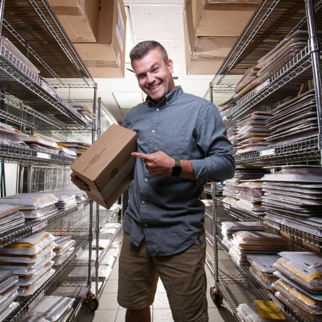 A Miller's team member holding a packed order box in the shipping racks, surrounded by orders waiting to go out