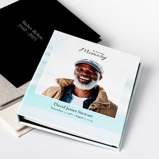 A memorial registration binder with a custom photograph cover reading In Loving Memory, stacked with black and linen covered binders