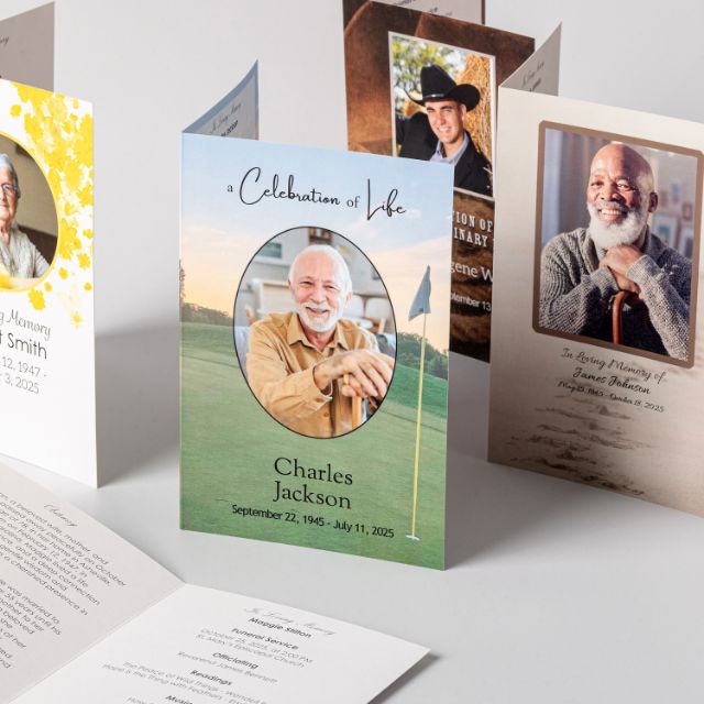 Several folded memorial service programs standing upright in different designs, one reading A Celebration of Life above a photograph, name, and dates