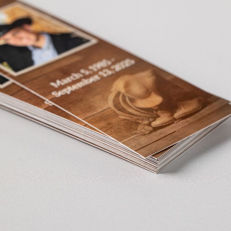 A stack of printed memorial bookmarks seen from the edge, showing the thickness of the felt press paper