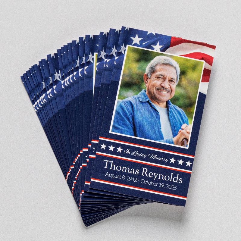 A fanned stack of memorial prayer cards in a patriotic design, each with a photograph, name, and dates