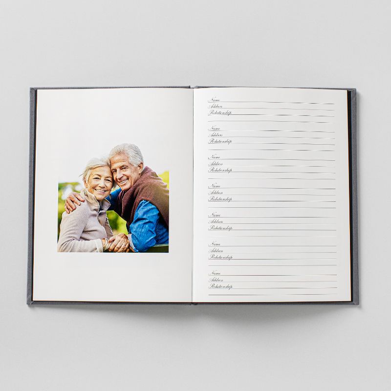 A memorial registration book lying open flat, a full-page photograph on the left and ruled lines for guest names, addresses, and relationships on the right