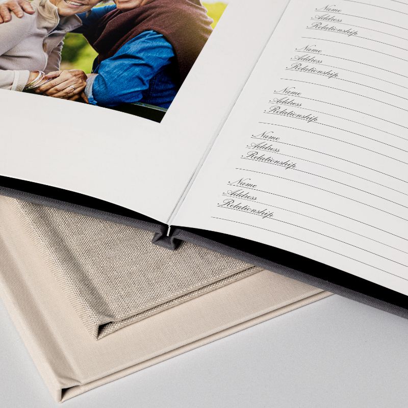 Close view of an open memorial registration book resting on a sand linen cover, its guest signing pages ruled for names and addresses