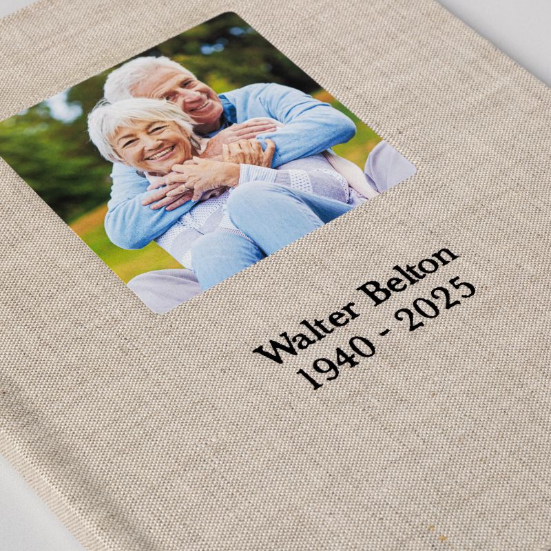 Close view of a sand linen registration book cover with a square cameo photograph above a debossed name and dates