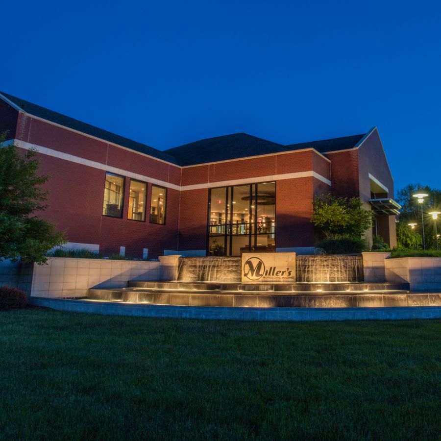 The brick entrance of the Miller's Professional Imaging lab in Columbia, Missouri, lit at dusk above its waterfall